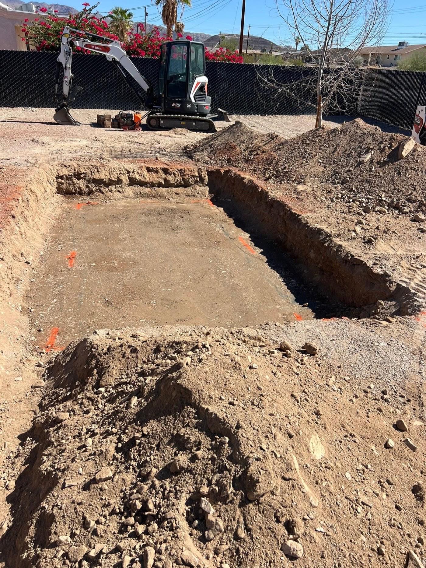 Excavator cutting and grading a staked pad on a Havasu Pavers job site in Lake Havasu City